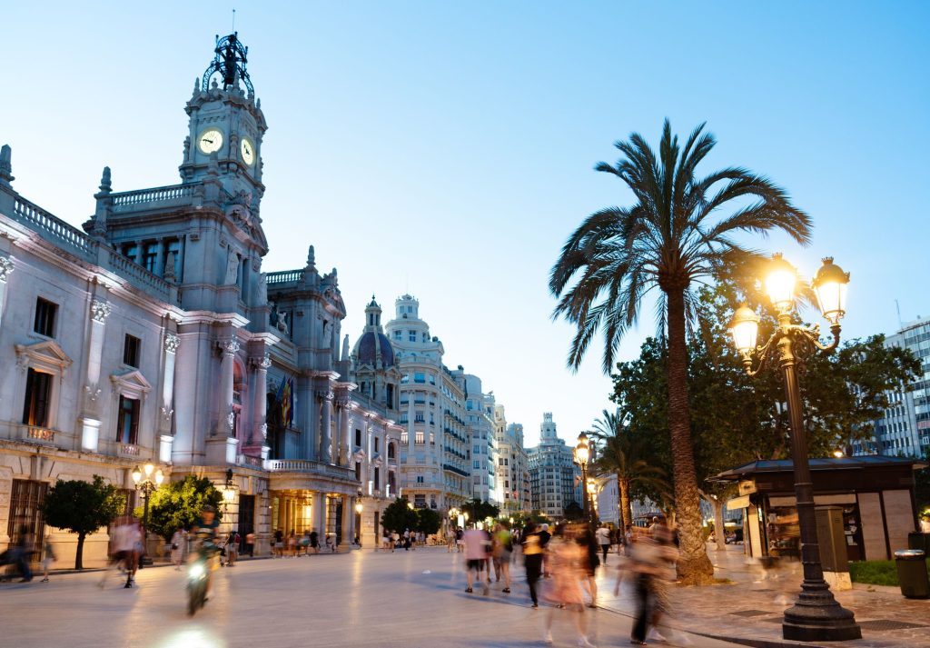 Plaza del Ayuntamiento in Valencia at sunset, warm evening light illuminating the historic buildings and city square.