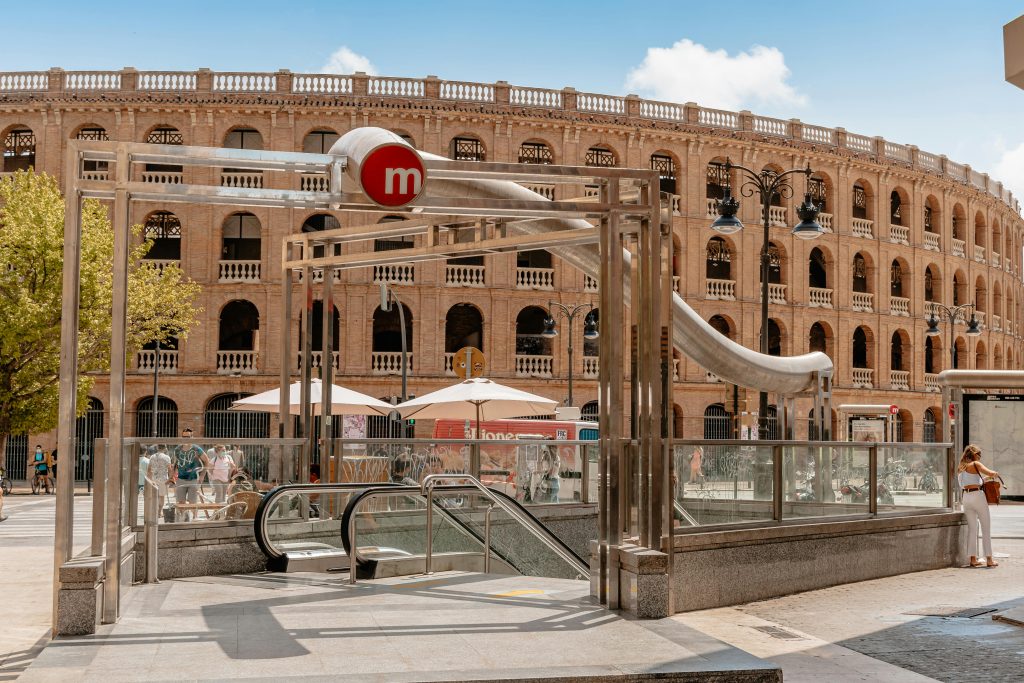 Historic circular brick building with arches and a metro entrance surrounded by palm trees in Valencia