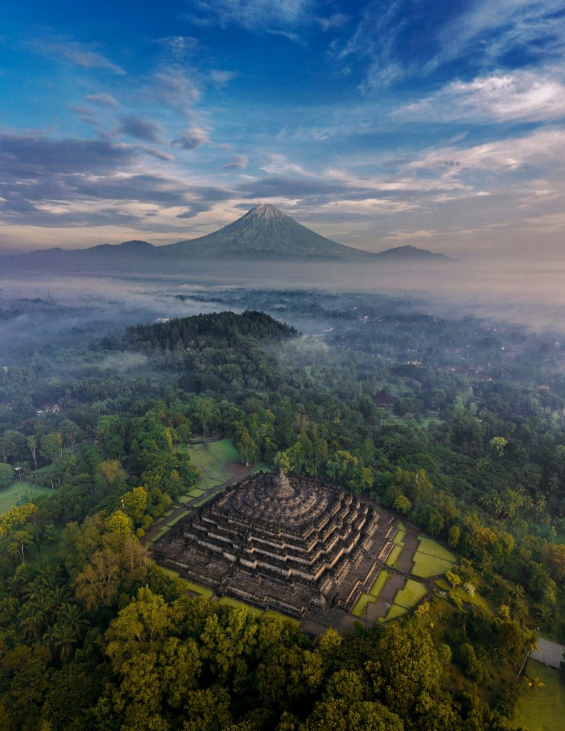 Aerial view of Borobudur Temple in Central Java, Indonesia, with a volcano in the distance