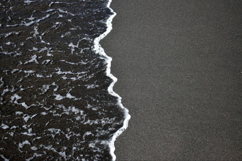 Ocean waves with white foam washing onto dark sand beach.