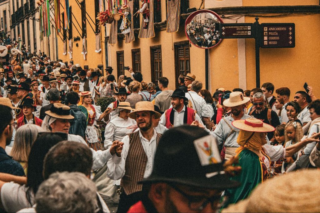A crowded street festival with people in traditional costumes dancing and walking through a narrow town street.